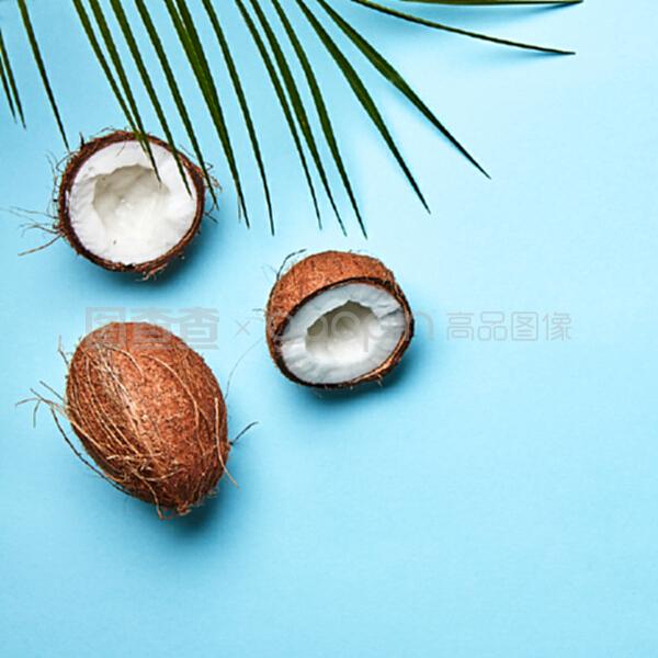整個和一半的椰子,在藍色背景上的棕櫚葉和文本空間的副本。一個奇異的水果。扁平放。一個椰子和棕櫚綠葉在藍色背景上的副本空間。熱帶堅果。扁平放。